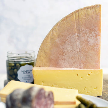 A board containing sliced salami, cornichons and blocks of cheese.