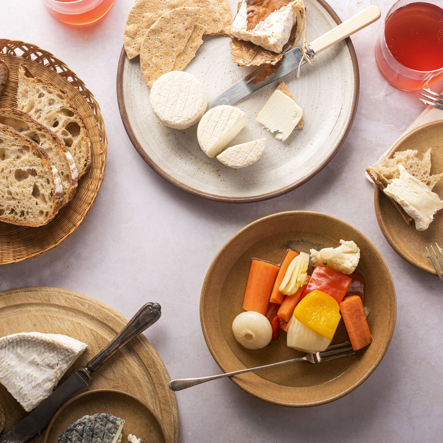 A table laid with plates of cheese, pickles, bread and glasses of wine.