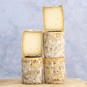 A stack of cut and whole barriquet goats cheese on a wooden board.