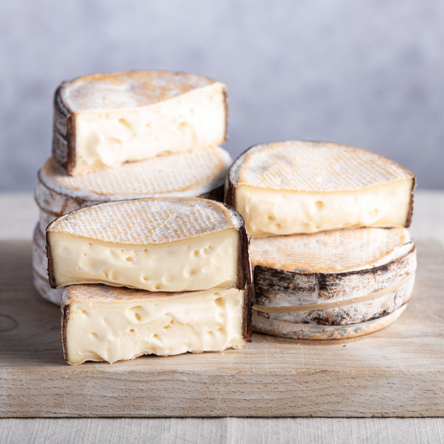 Cut and whole pieces of Little Rollright cheese on a wooden chopping board.