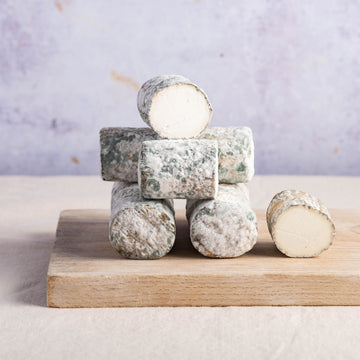 Cuts and whole pieces of Elrick Log goat's cheese stacked on a wooden board.