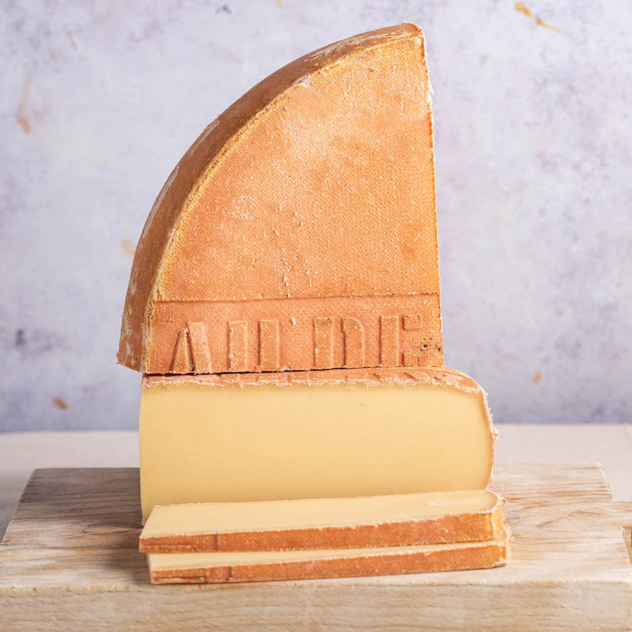 Slices and large cuts of Raclette cheese on a wooden chopping board.