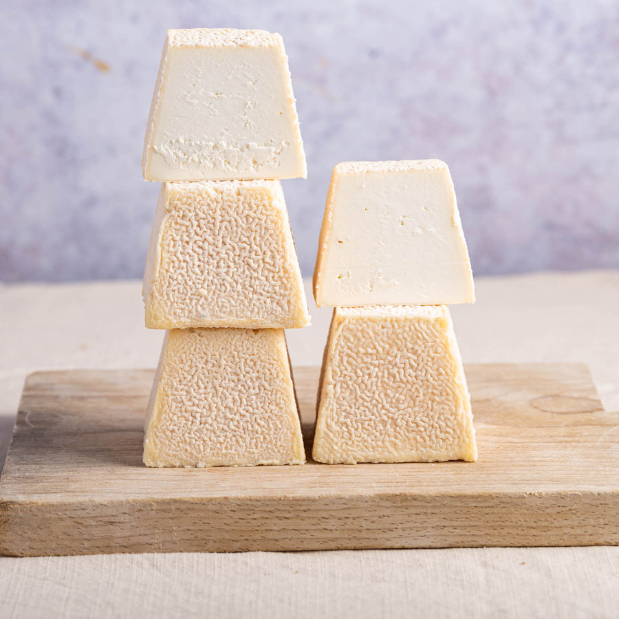 Cut and whole sinodun hill goat cheese stacked up on a wooden board.