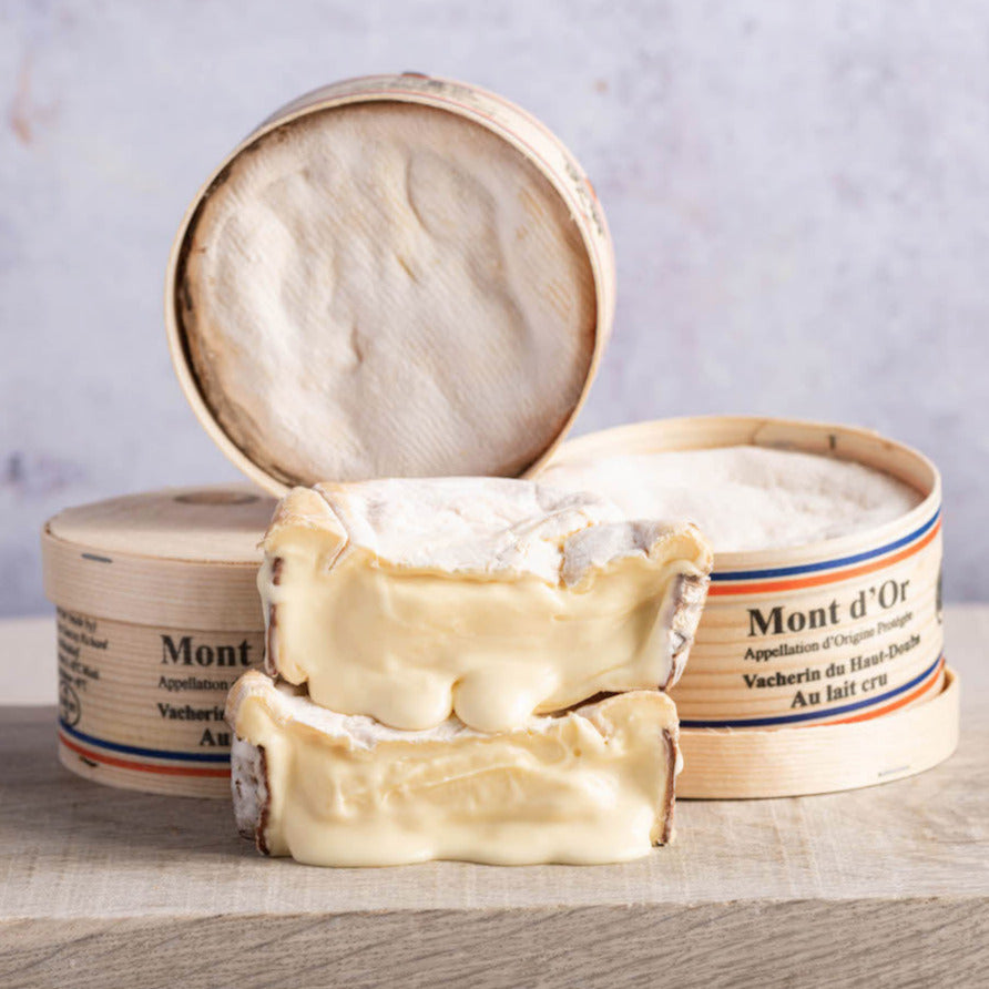 Cut and whole Vacherin Mont d'Or cheeses on a wooden board.