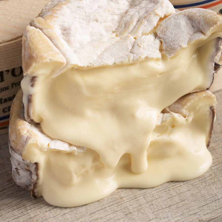 Oozing, soft cuts of Vacherin cheese on a wooden board.